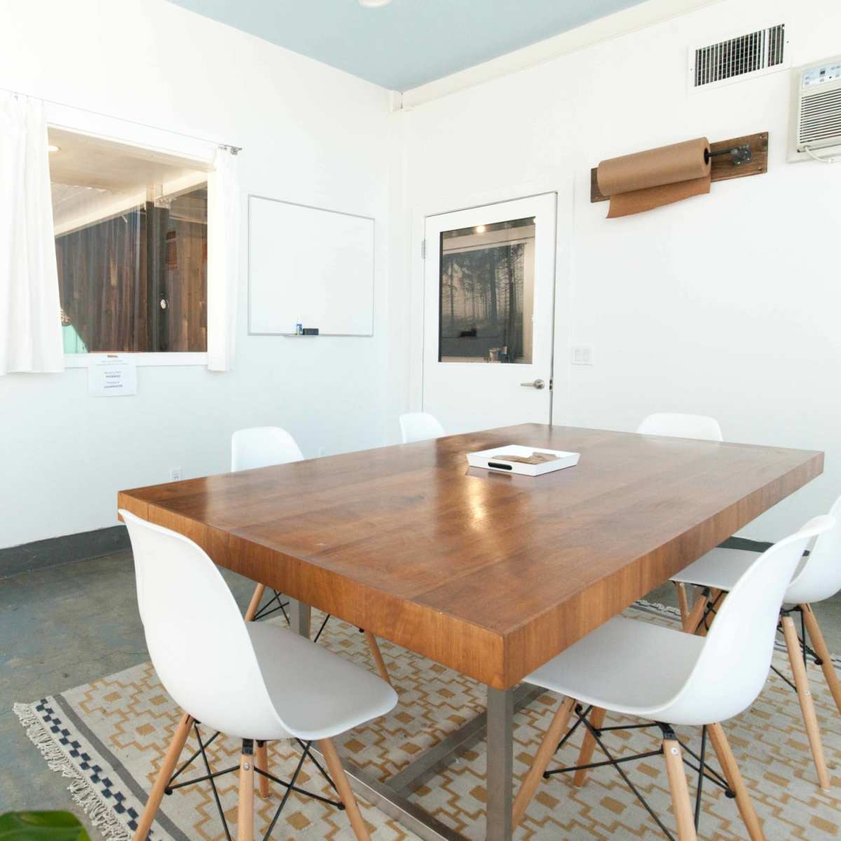 A conference room features a wooden table surrounded by white chairs, a television mounted on the wall, and a whiteboard.