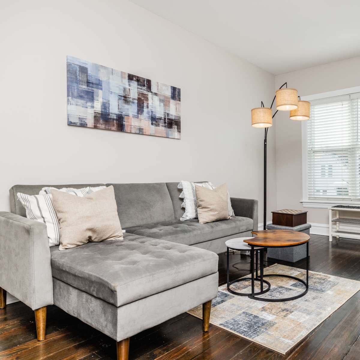 A modern living room featuring a gray sectional sofa, a circular coffee table, and a large window with blinds.