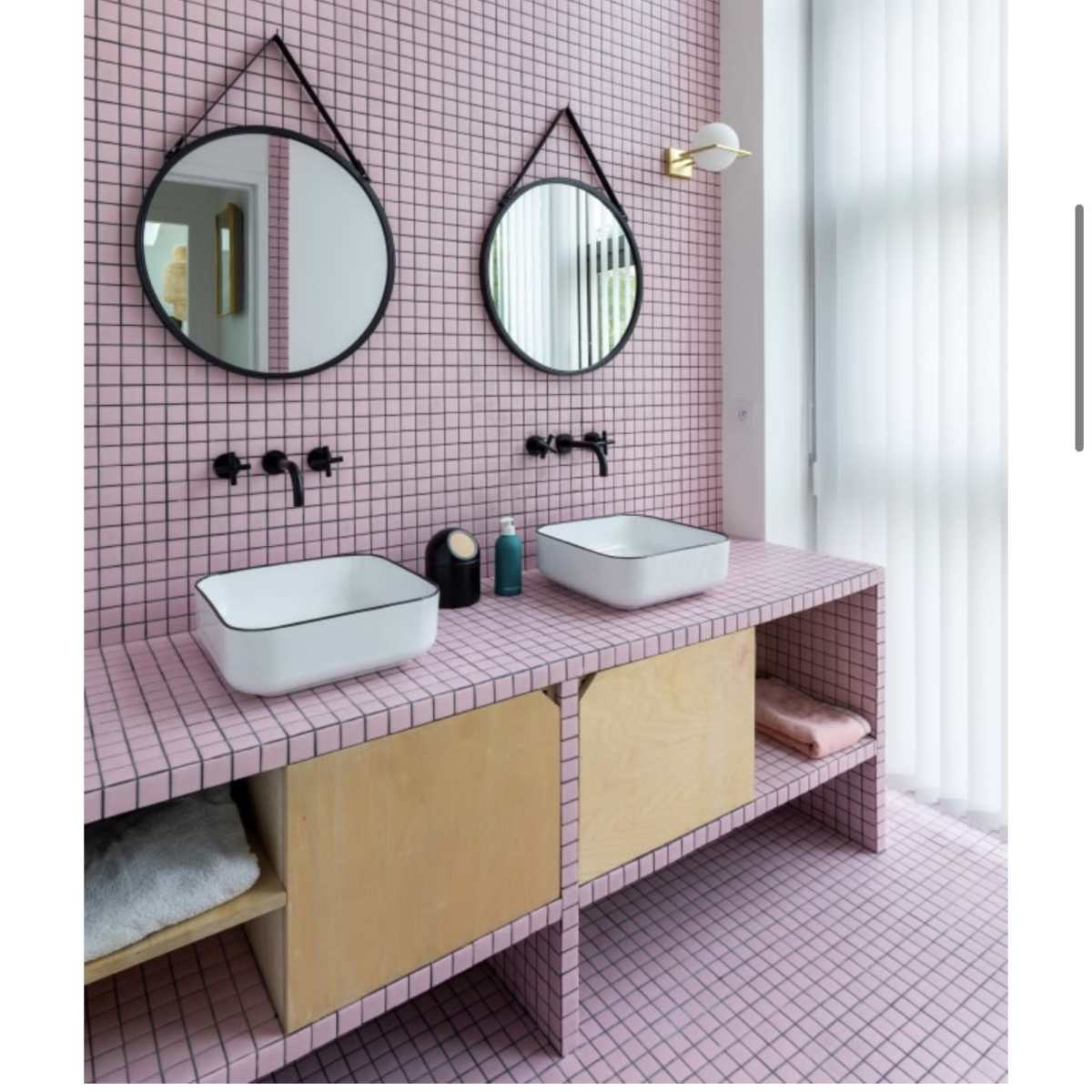 A bathroom with pink tiled walls, two round mirrors, and a wooden vanity featuring two modern sinks.