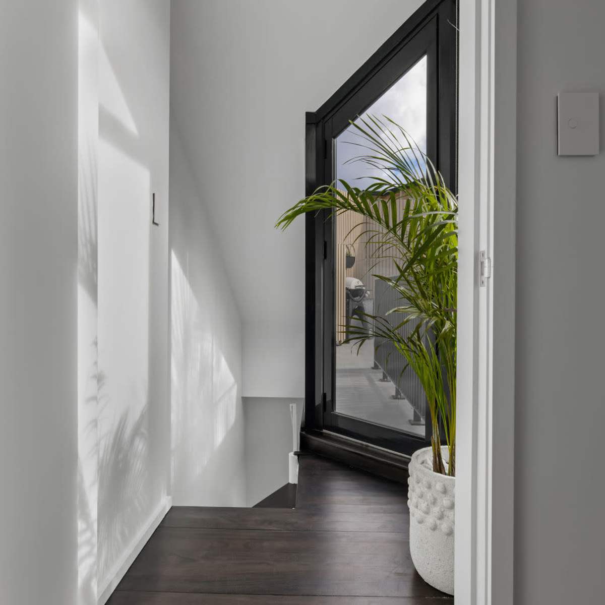 A hallway featuring a large window with a view of a potted plant and light wood flooring.