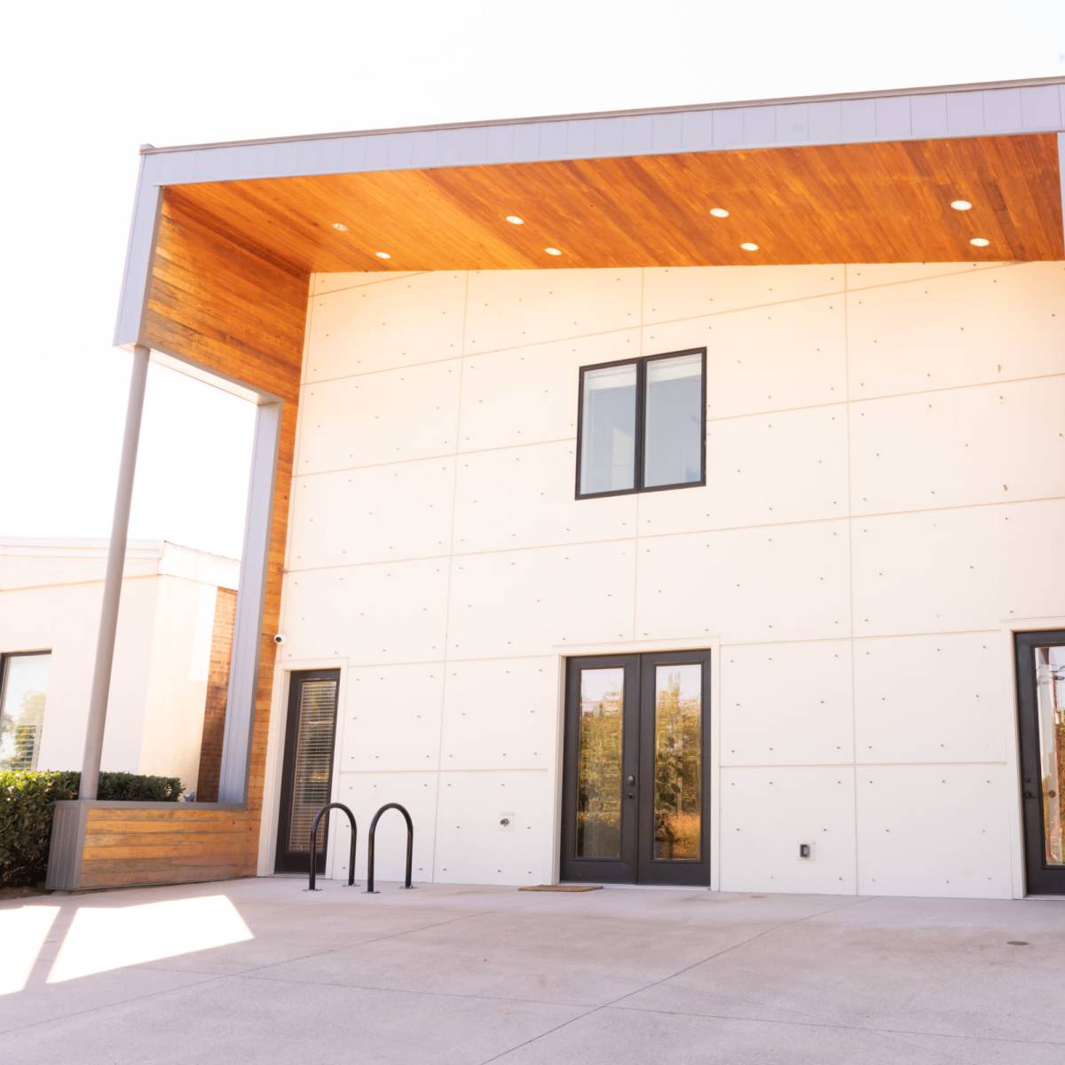 A modern, two-story building with a concrete exterior and a wooden overhang at the entrance.