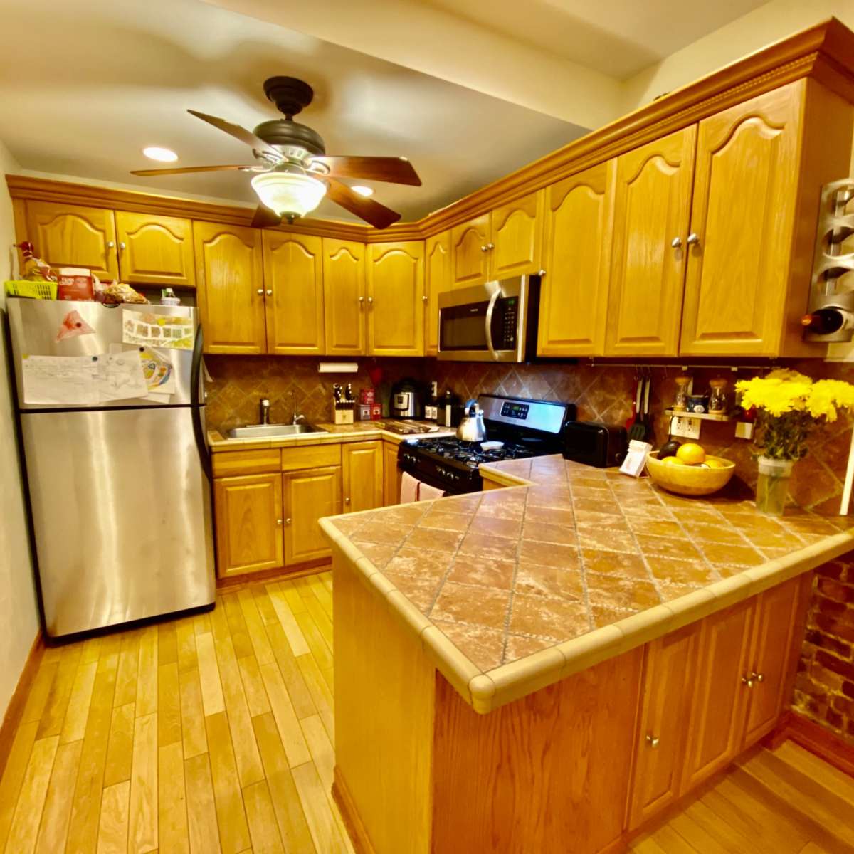 The kitchen features wooden cabinetry, a stainless steel refrigerator, and a tile countertop with a small dining area.