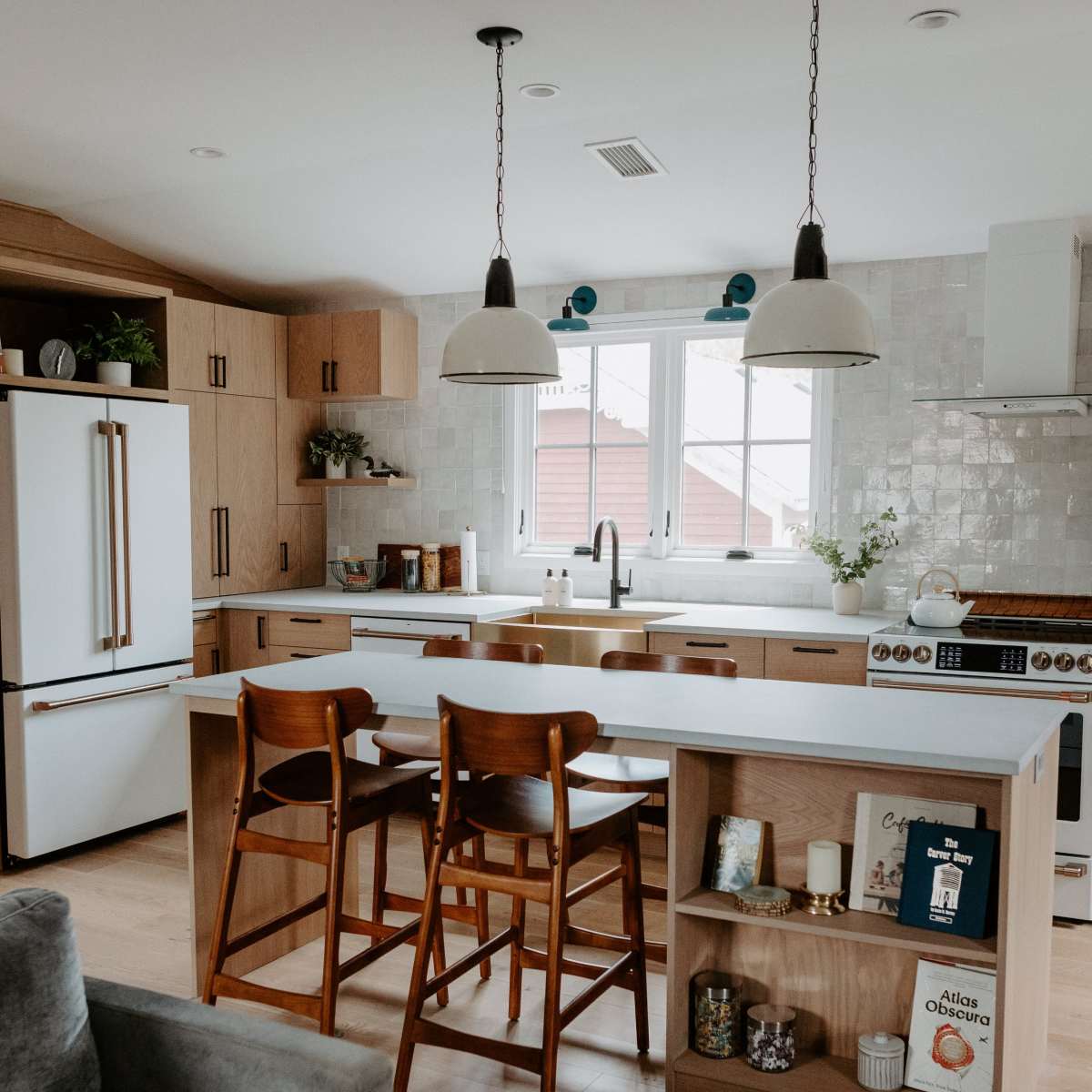 A modern kitchen features wooden cabinets, a large island with bar stools, and a window above the sink.