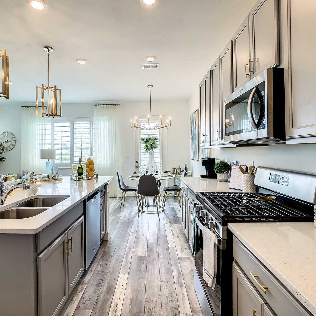A modern kitchen featuring gray cabinets, stainless steel appliances, and a dining area with a glass table and stylish light fixtures.