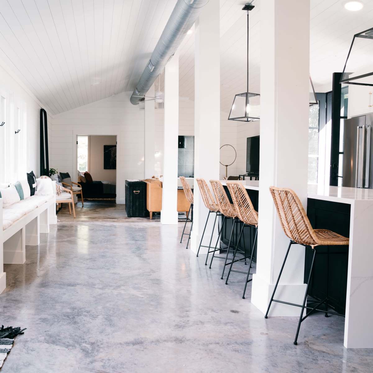 A modern interior space featuring a kitchen with bar stools, a dining area, and large windows allowing natural light to fill the room.