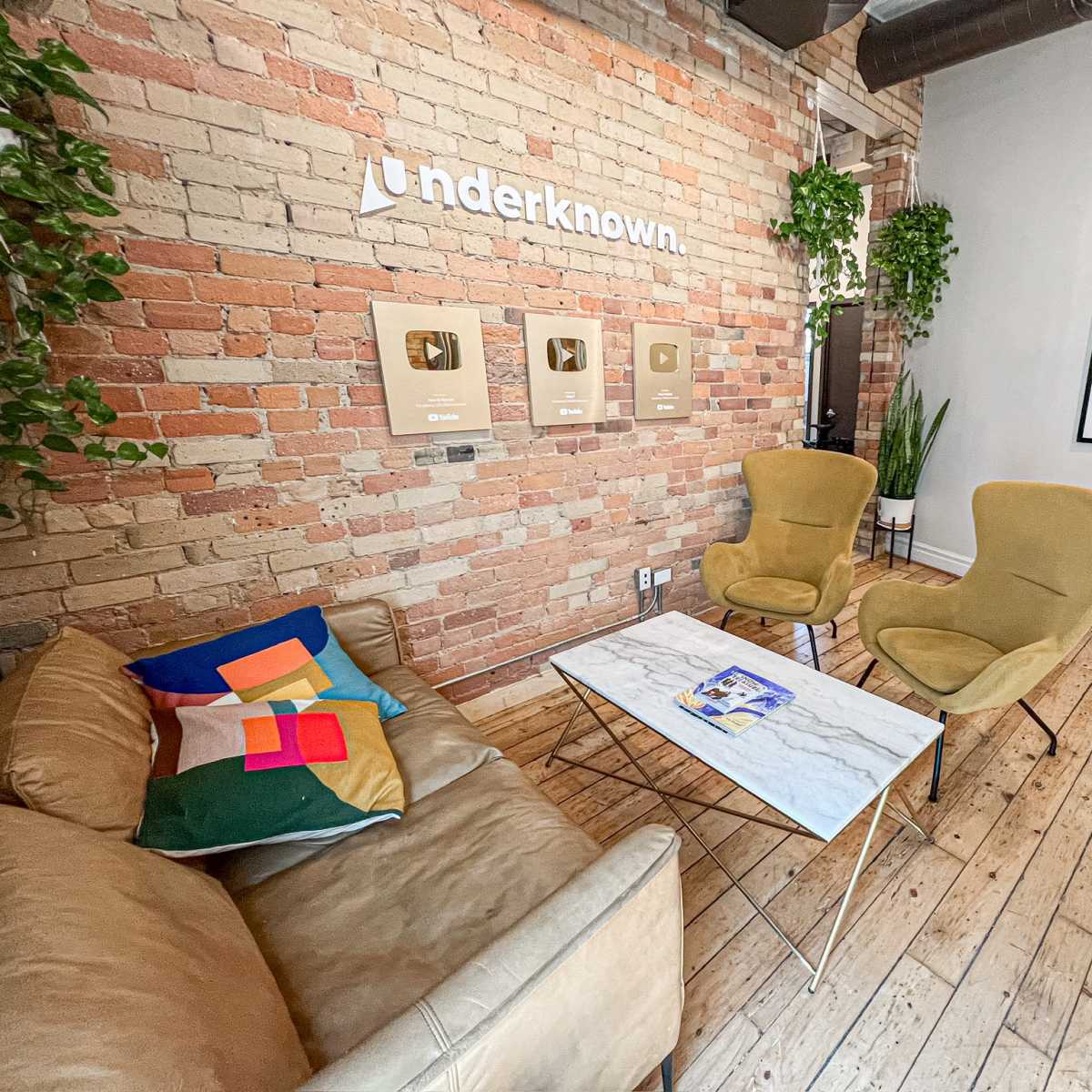 A modern lounge area with a brick wall, two armchairs, a couch, and a coffee table displaying framed awards.