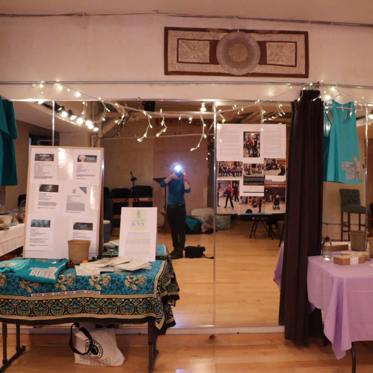 A room with mirrors, decorated with string lights, displaying informational posters and colorful tablecloths.