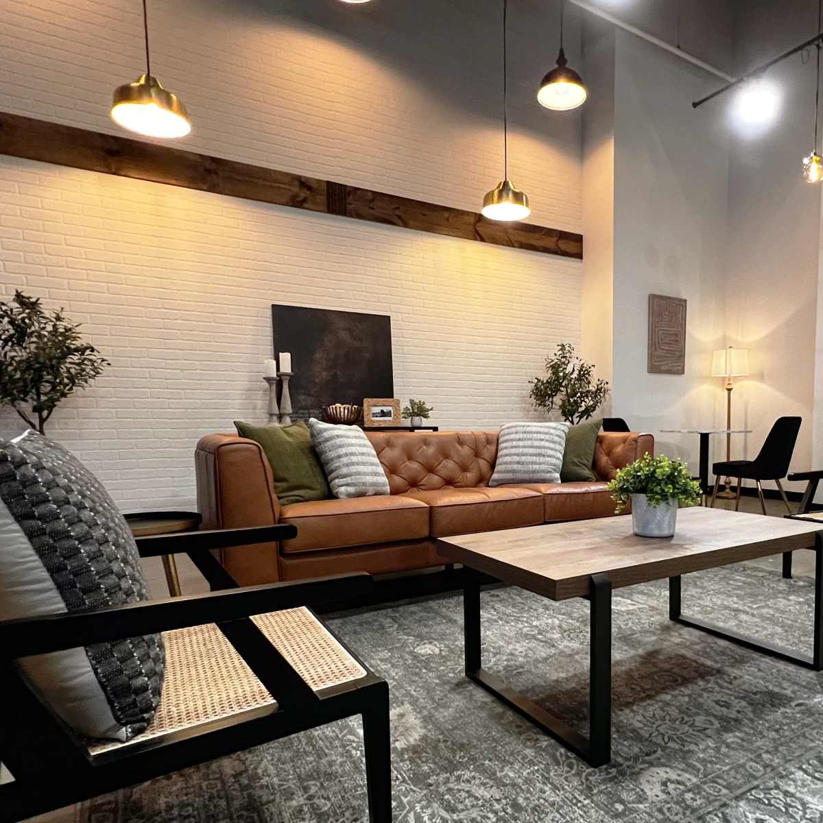 A modern living room with a leather sofa, two upholstered chairs, a coffee table, and a fireplace against a white brick wall.