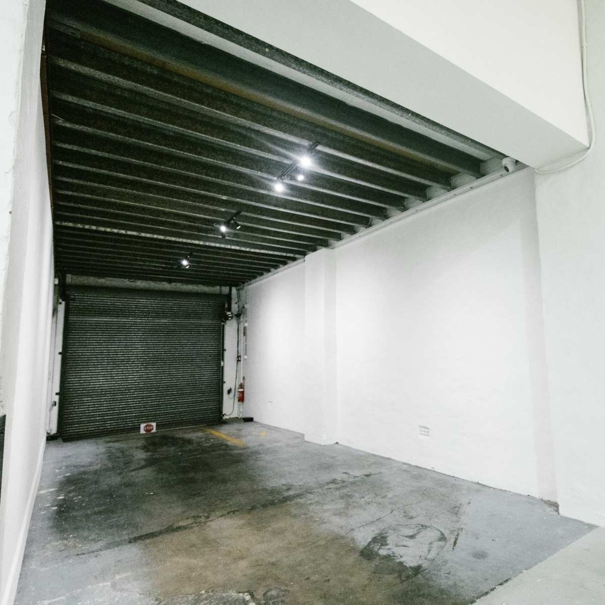 An empty industrial space with grey concrete flooring, white walls, and a closed metal roll-up door at one end.