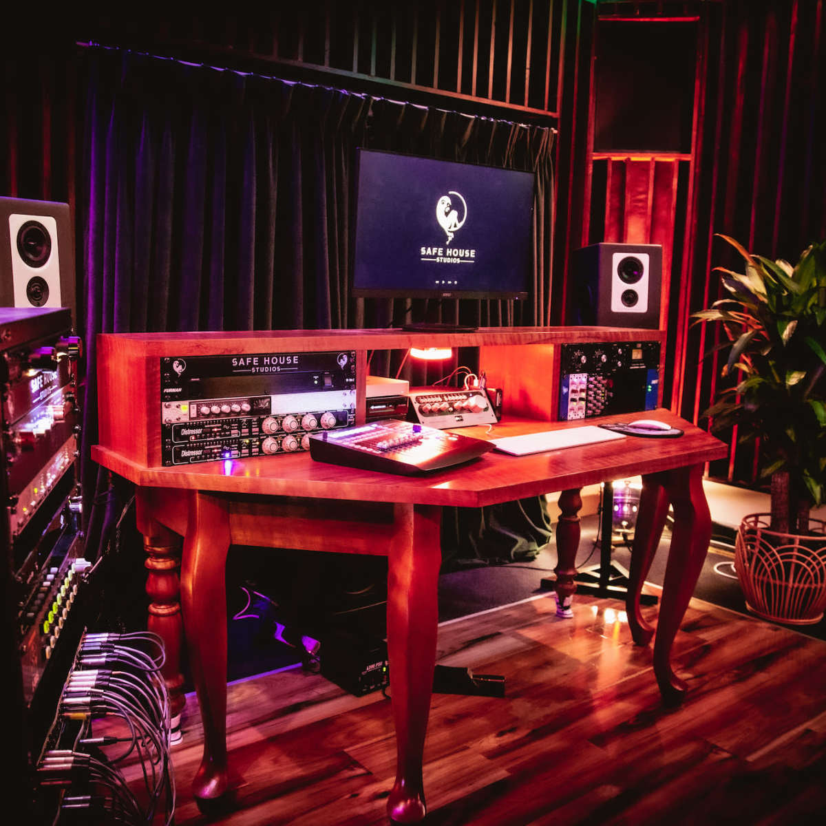 A music production studio featuring a wooden desk with audio equipment, speakers, and a computer monitor in a dimly lit room.