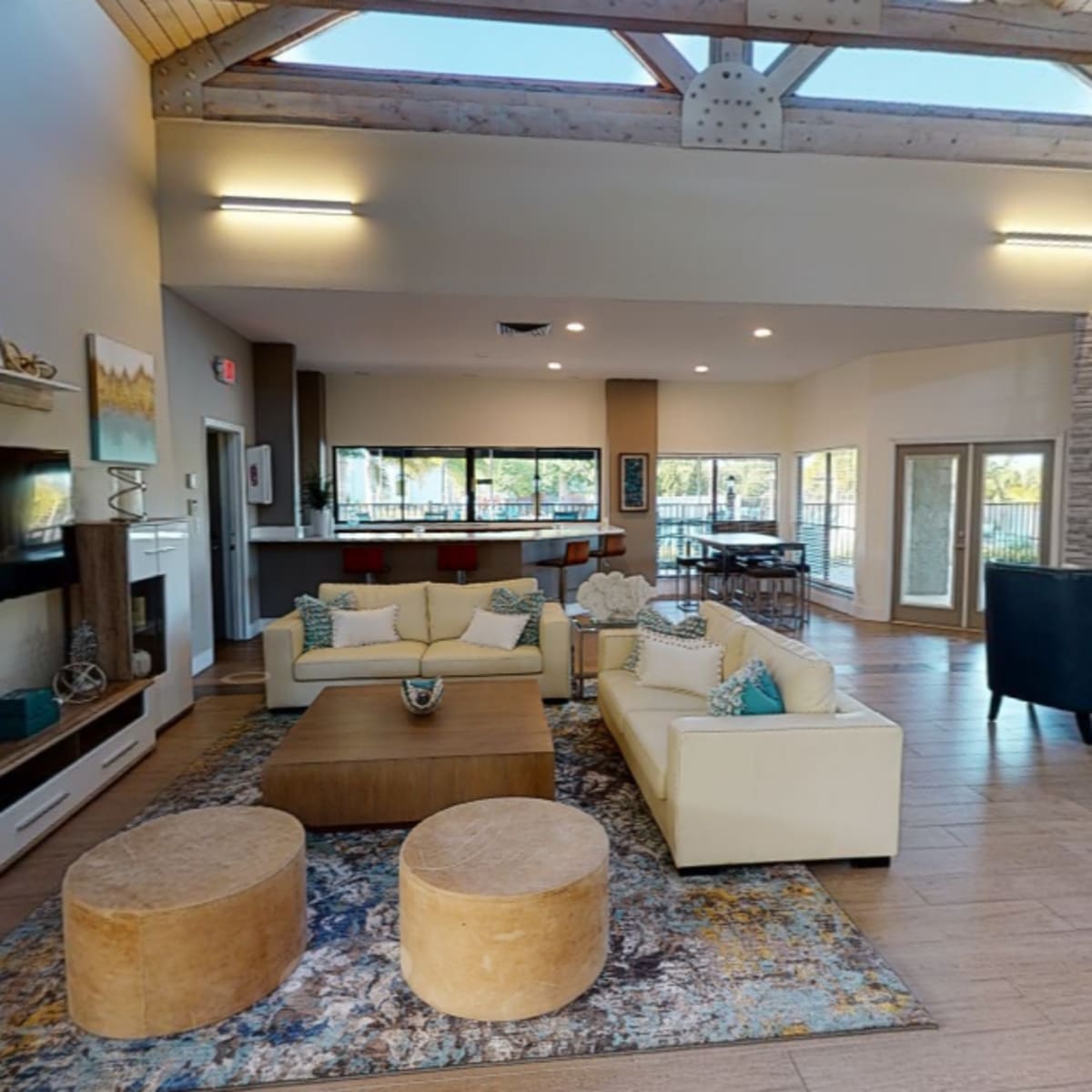 A modern living room with a high ceiling, light-colored furniture, a large area rug, and large windows letting in natural light.