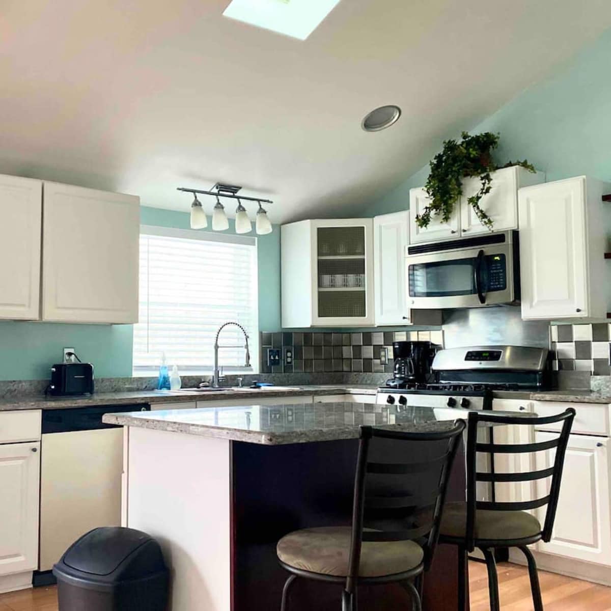 A modern kitchen with white cabinets, a granite countertop, a black refrigerator, and stainless steel appliances.