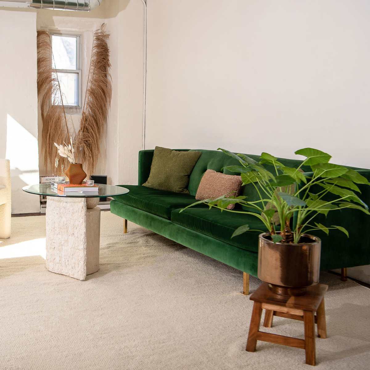 A modern living space featuring a green sofa, two unique side tables made of marble and stone, a potted plant, and decorative elements on a light-colored rug.