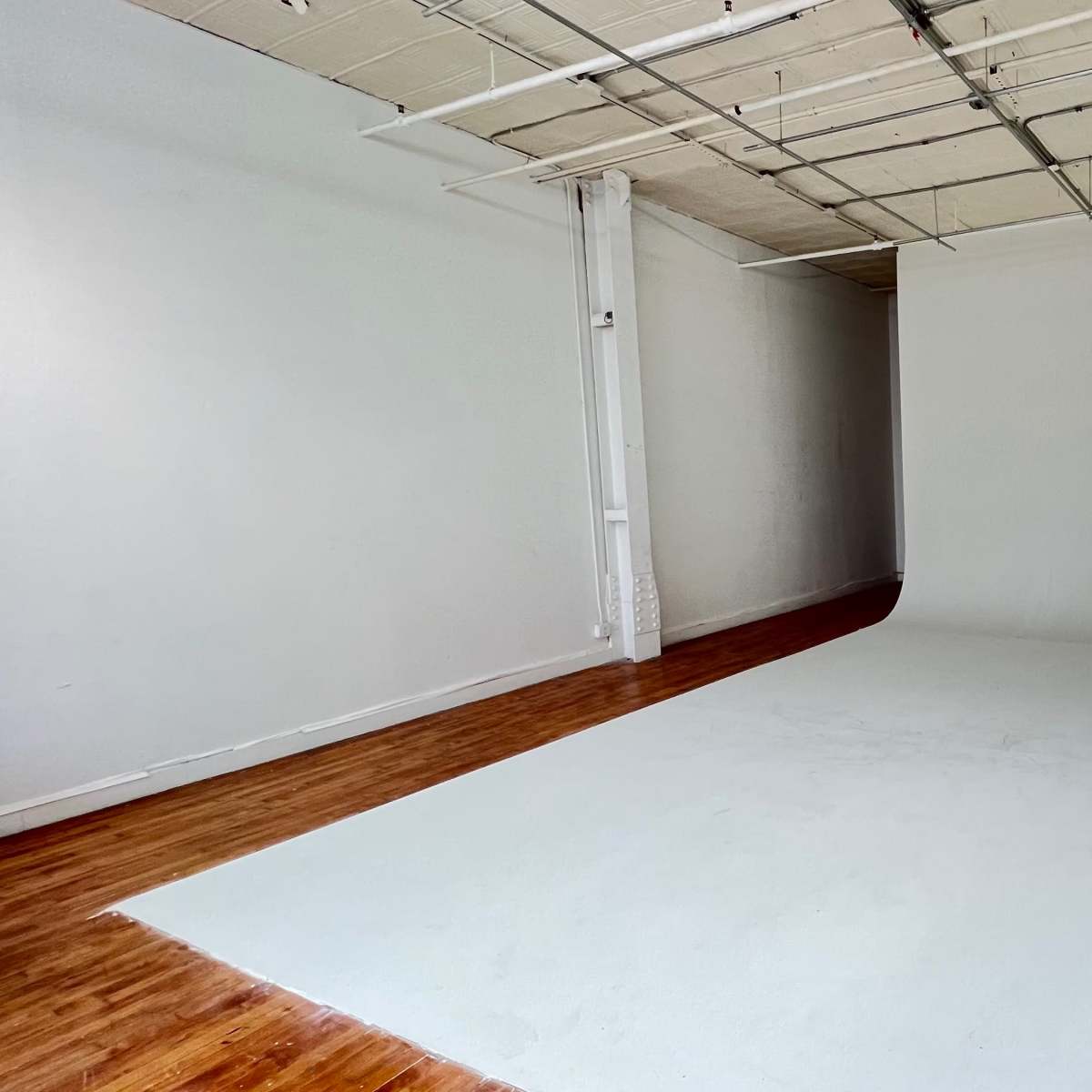 An empty studio space with a white cyc wall and wooden flooring.