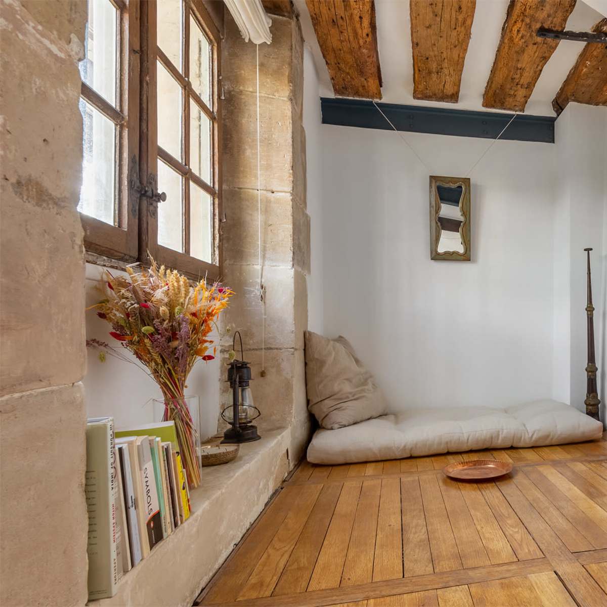 A minimalist room with wooden beams, a cushioned seating area, a mirrored wall, and stacked circular storage containers.