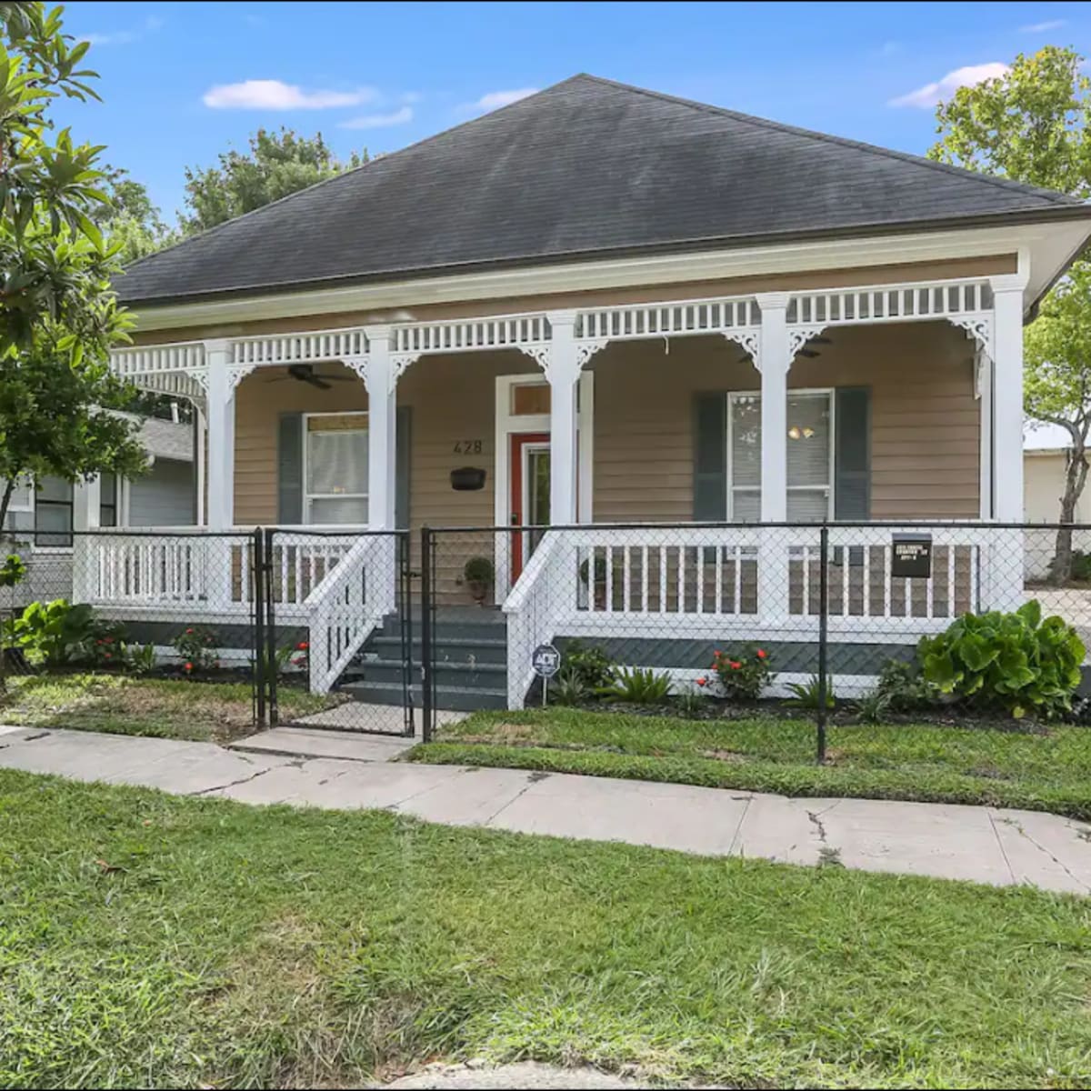 A single-story house with a covered front porch, white railings, and a fenced yard.