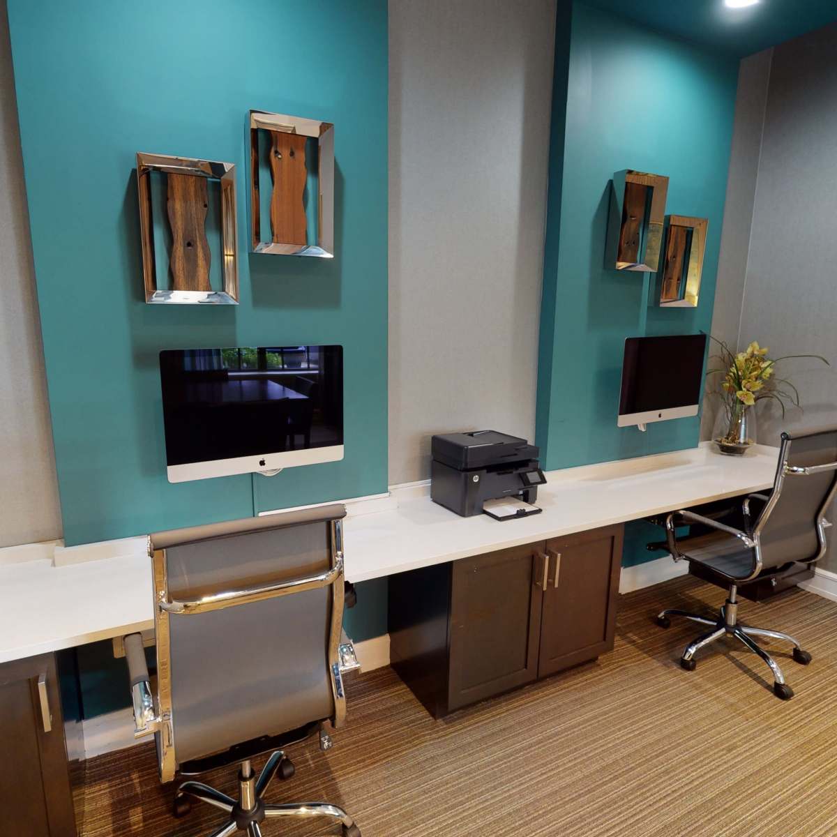 A modern office space featuring two computer workstations with matching monitors, a printer, and decorative wall-mounted shelves.