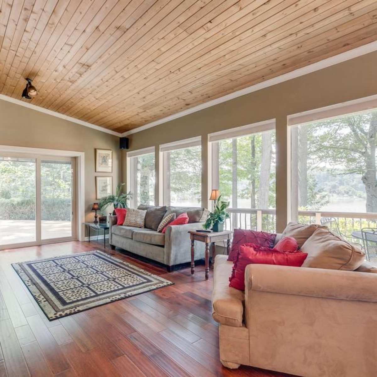 A living room with wooden ceilings, large windows providing a view of the outdoors, and a stone fireplace.