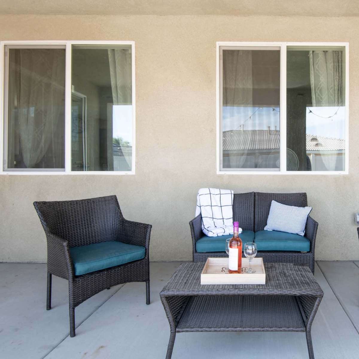 A set of wicker patio furniture, including two armchairs and a couch, is arranged around a coffee table on a concrete patio.