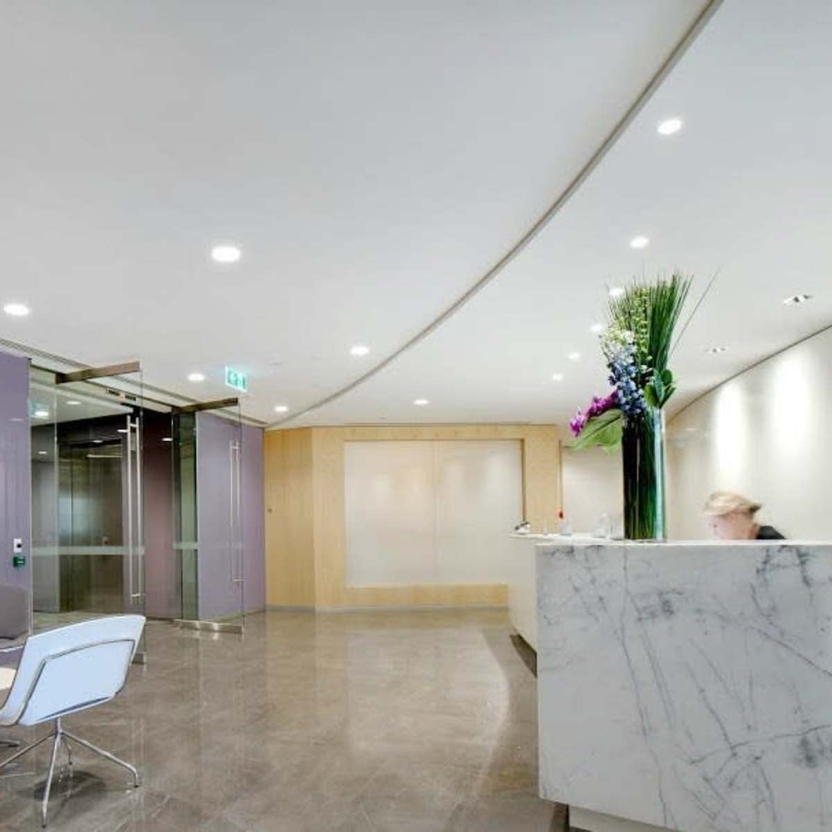 A modern office reception area featuring a marble front desk, minimalist seating, and a large flower arrangement.