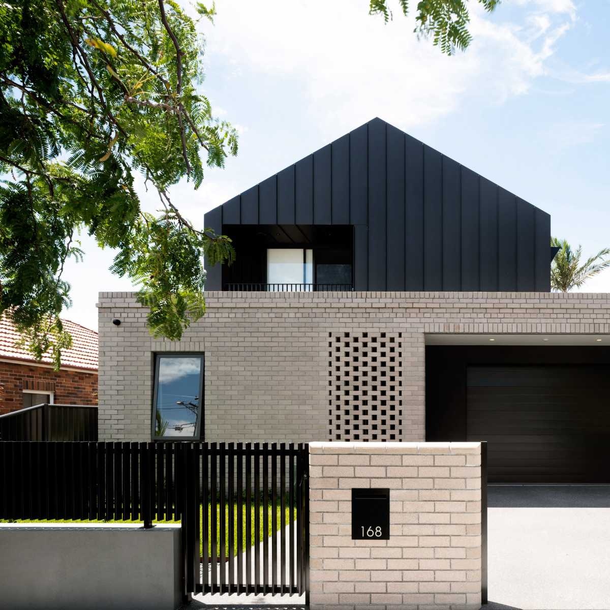 A modern two-story house with a combination of brick and black metal siding, featuring a driveway and a decorative fence.