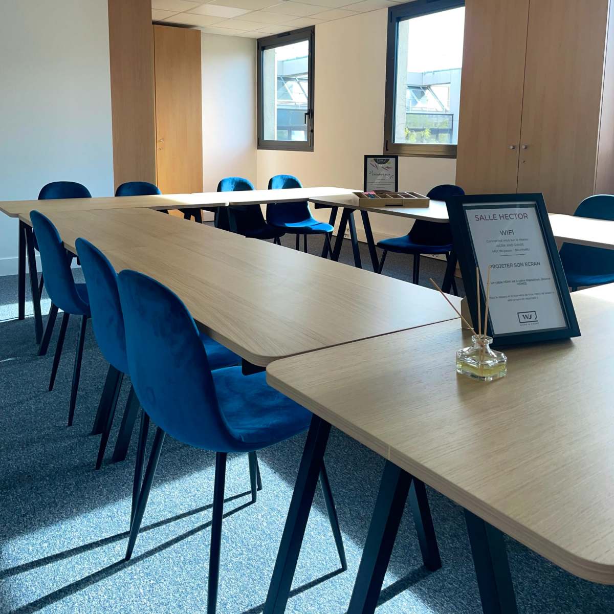 A meeting room features wooden tables arranged in a U-shape with blue chairs, along with a sign indicating Wi-Fi details.