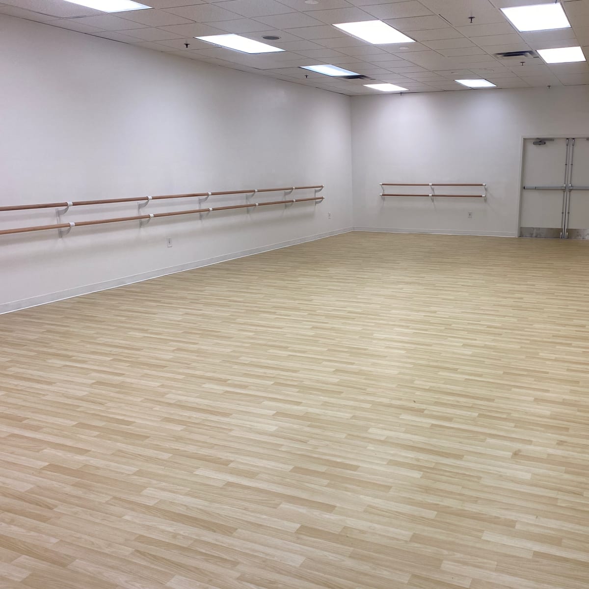 A dance studio with wooden flooring, mirrored walls, and barre installations along one side.