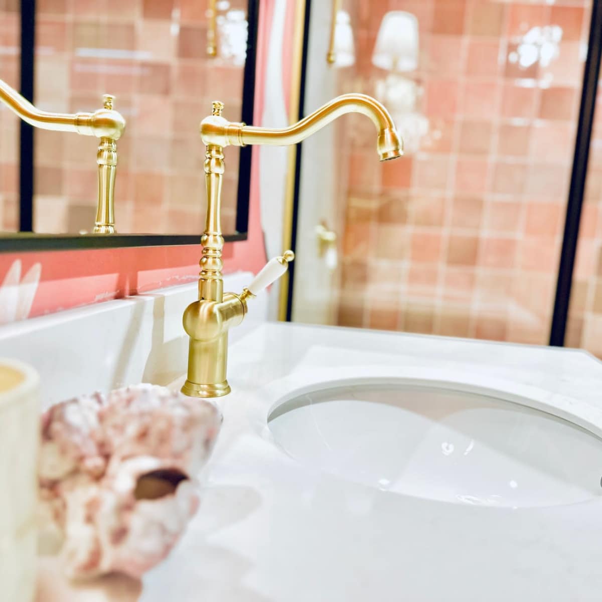 A close-up view of a modern bathroom sink with a gold faucet and a shell placed beside it.