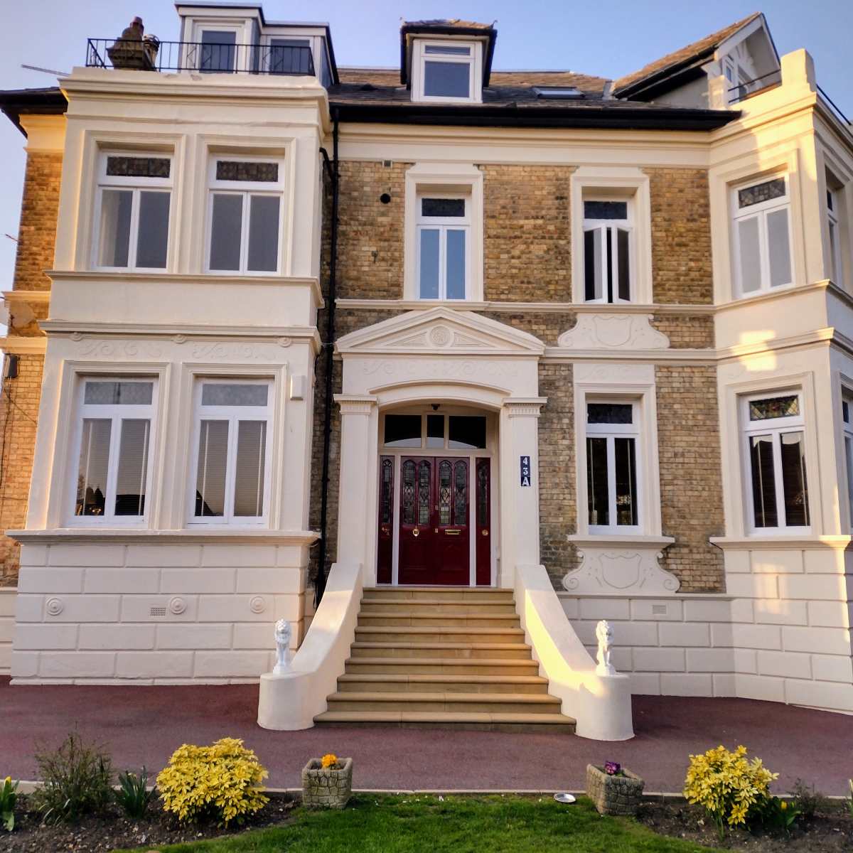 A large, three-story brick house with a white exterior, ornate detailing, and a red double door entrance.