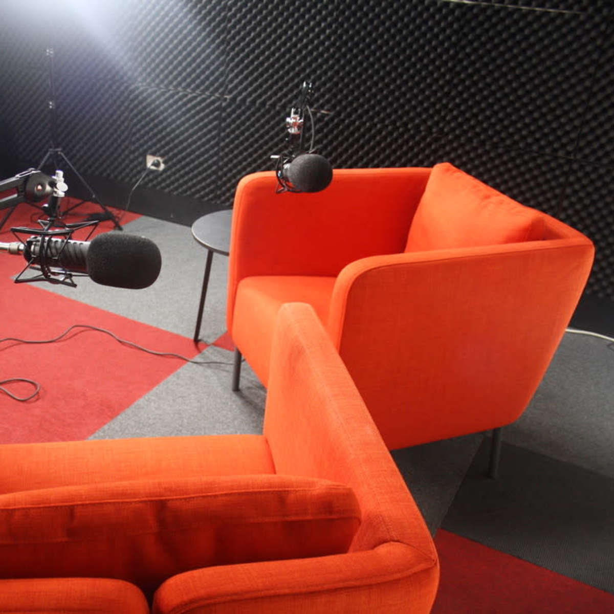 Two orange chairs facing each other in a studio setup with microphones and soundproofing materials in the background.