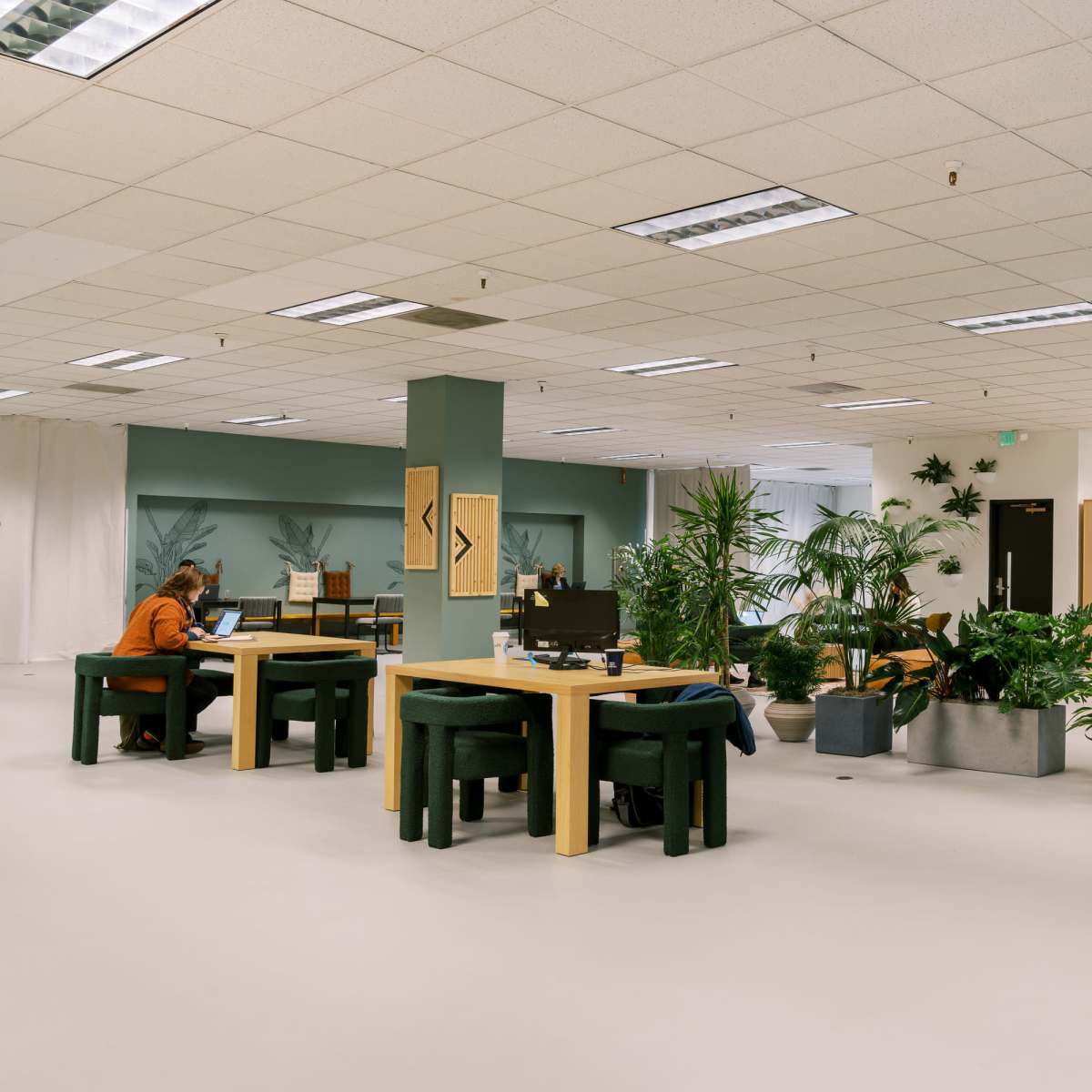 A spacious office environment with several desks, plants, and seating areas for working.