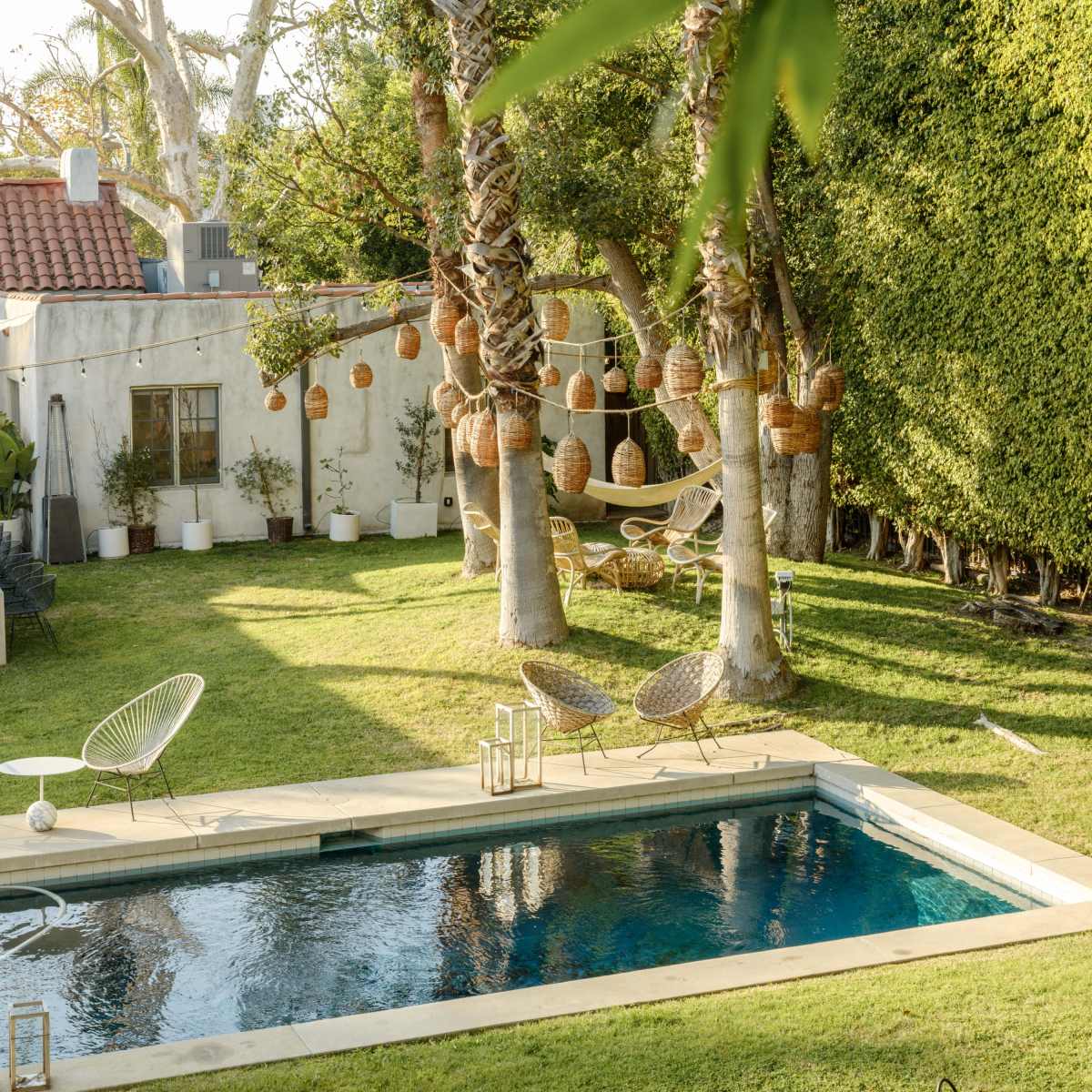 A backyard with a swimming pool, surrounded by palm trees, hanging baskets, and a hammock.