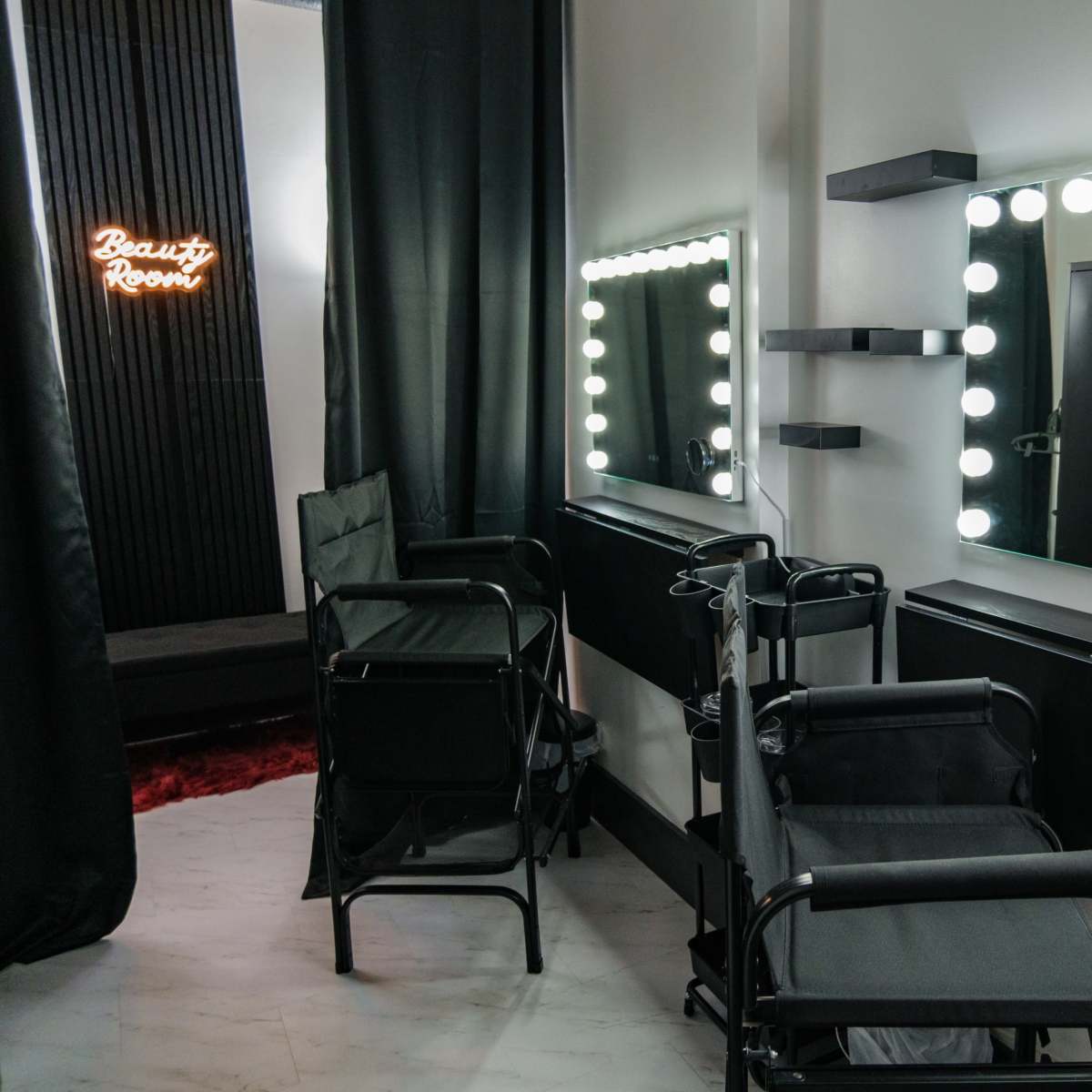 A beauty room featuring two illuminated mirrors with ring lights, two styling chairs, and black decor.