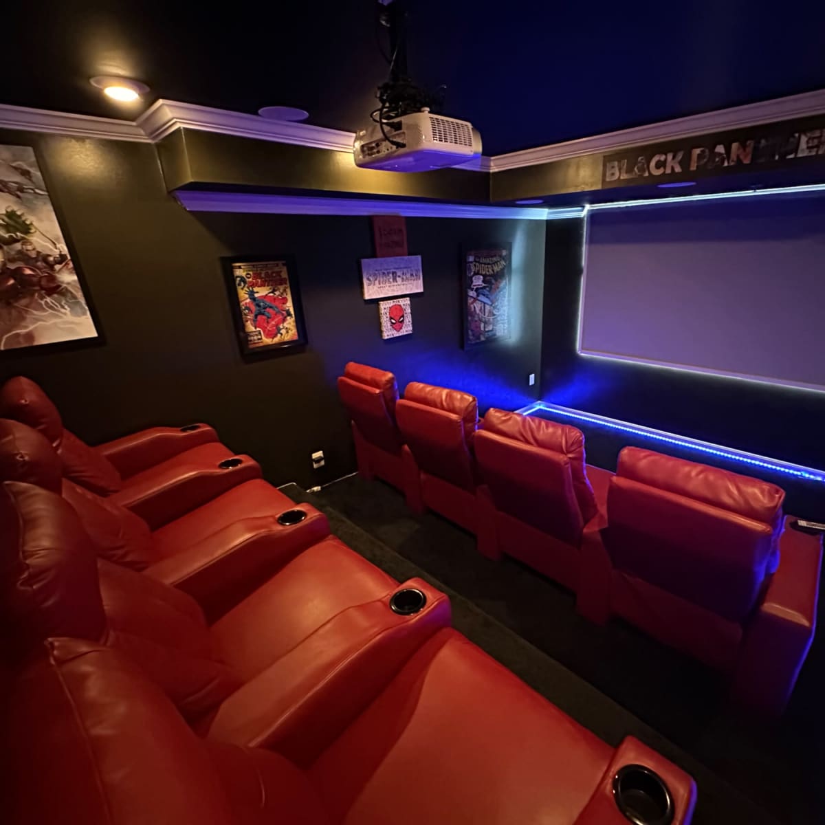A home theater with red recliner seating, a large movie screen, and superhero-themed artwork on the walls.