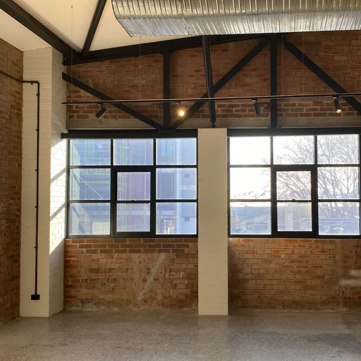 An interior space with exposed brick walls, large windows providing natural light, and a white partition.