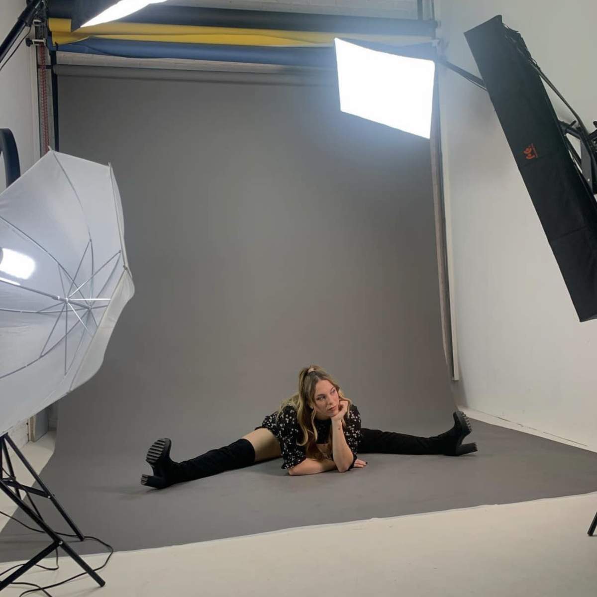 A person is posing on a gray backdrop in a photography studio with multiple lights set up around them.