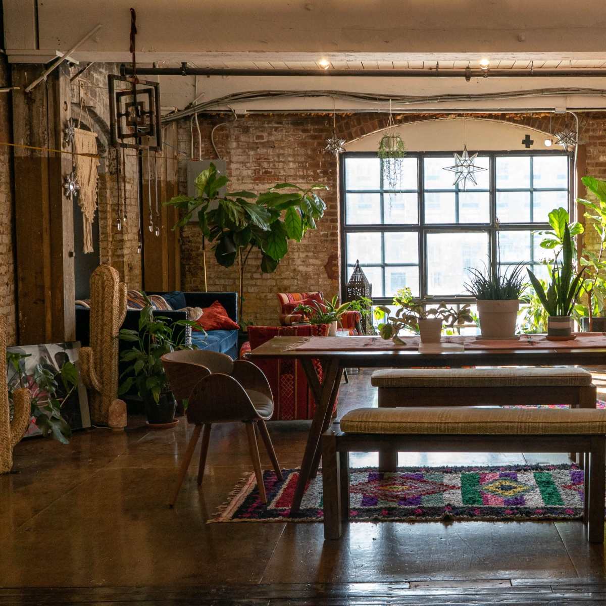 A spacious, well-lit room with a long wooden table and various plants, featuring a blend of modern and rustic decor.