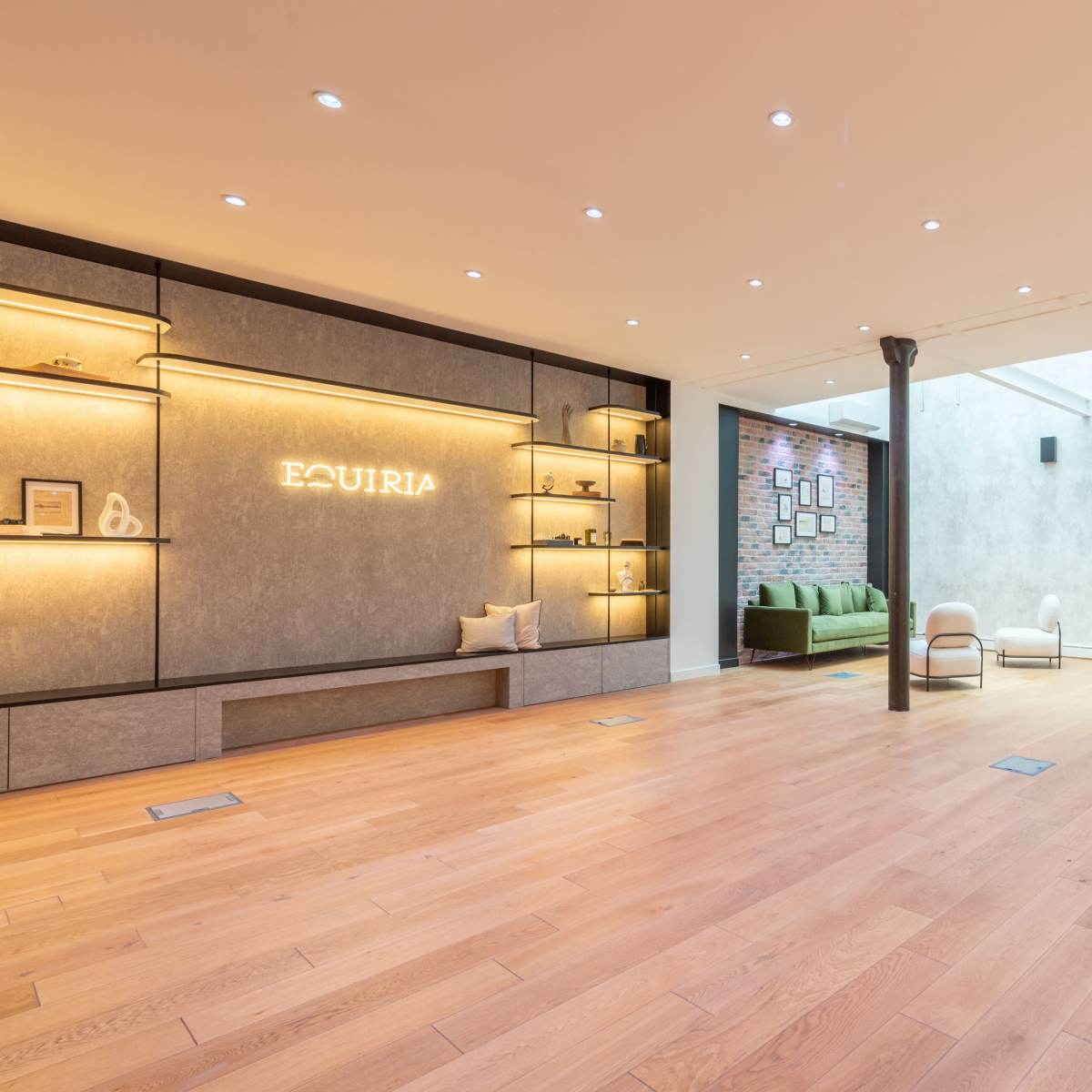 A modern, minimalistic interior space with wooden floors, wall shelves illuminated with warm lighting, and a green couch along the back wall.