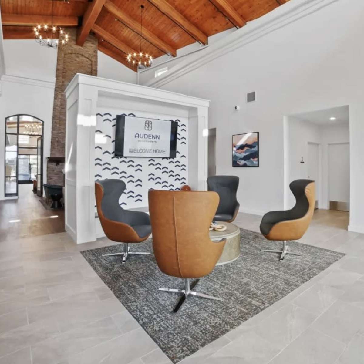 A lobby area with modern seating arrangements, a rug, and a decorative wall feature, all under a high wooden ceiling.