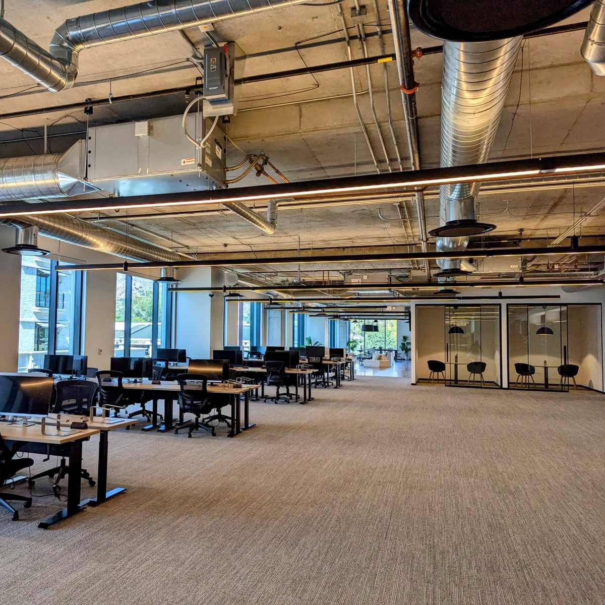 A spacious office interior with rows of desks, computers, and large windows allowing natural light.