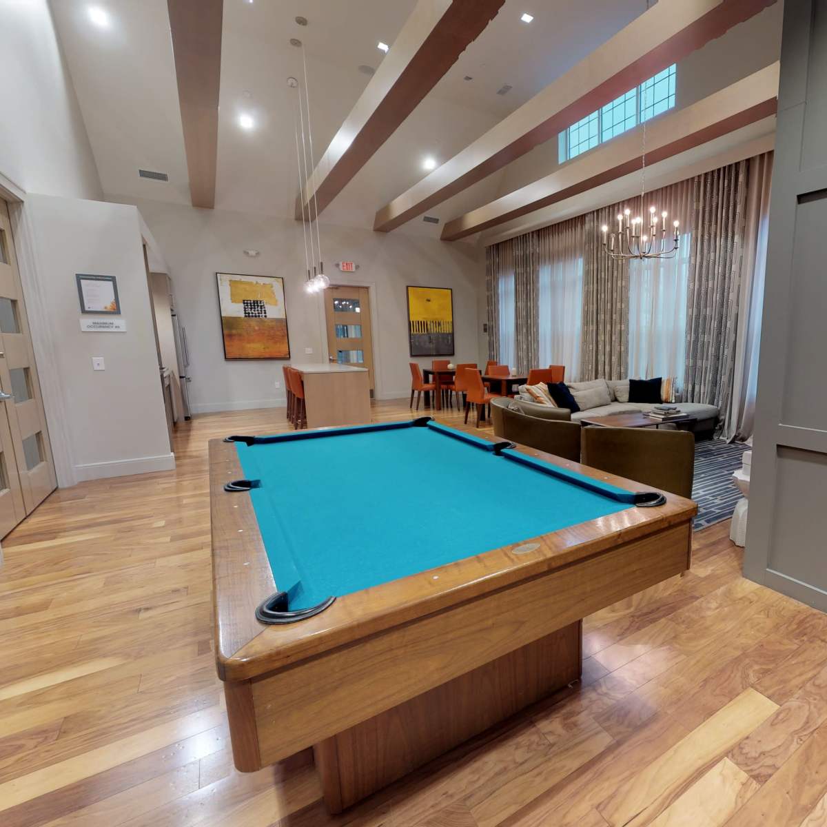 A recreational room featuring a slate pool table with a turquoise felt surface, wooden flooring, and a seating area in the background.