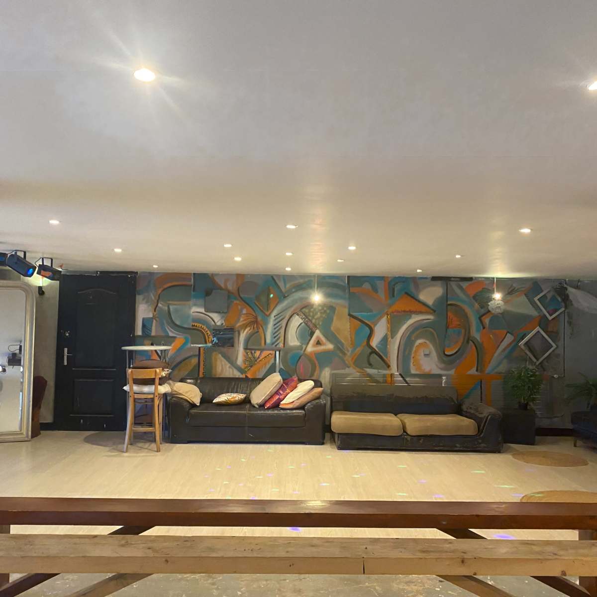 An indoor lounge area with a colorful mural on the wall, several couches, and a wooden table in the foreground.