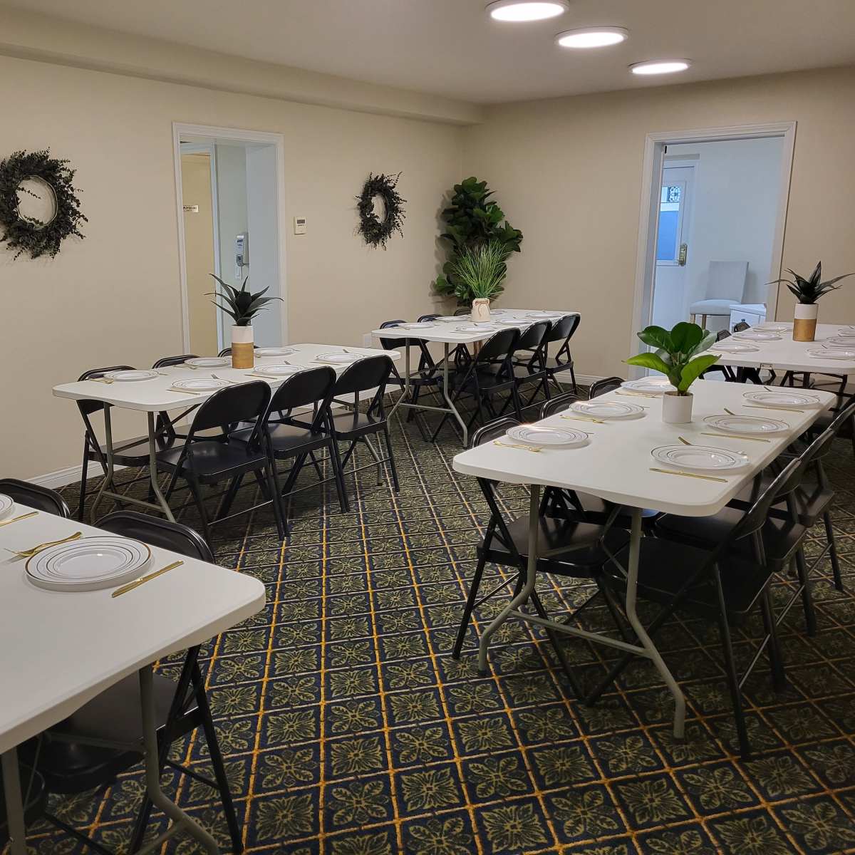 A neatly arranged dining area with multiple tables set for a meal, complete with decorative plants and place settings.