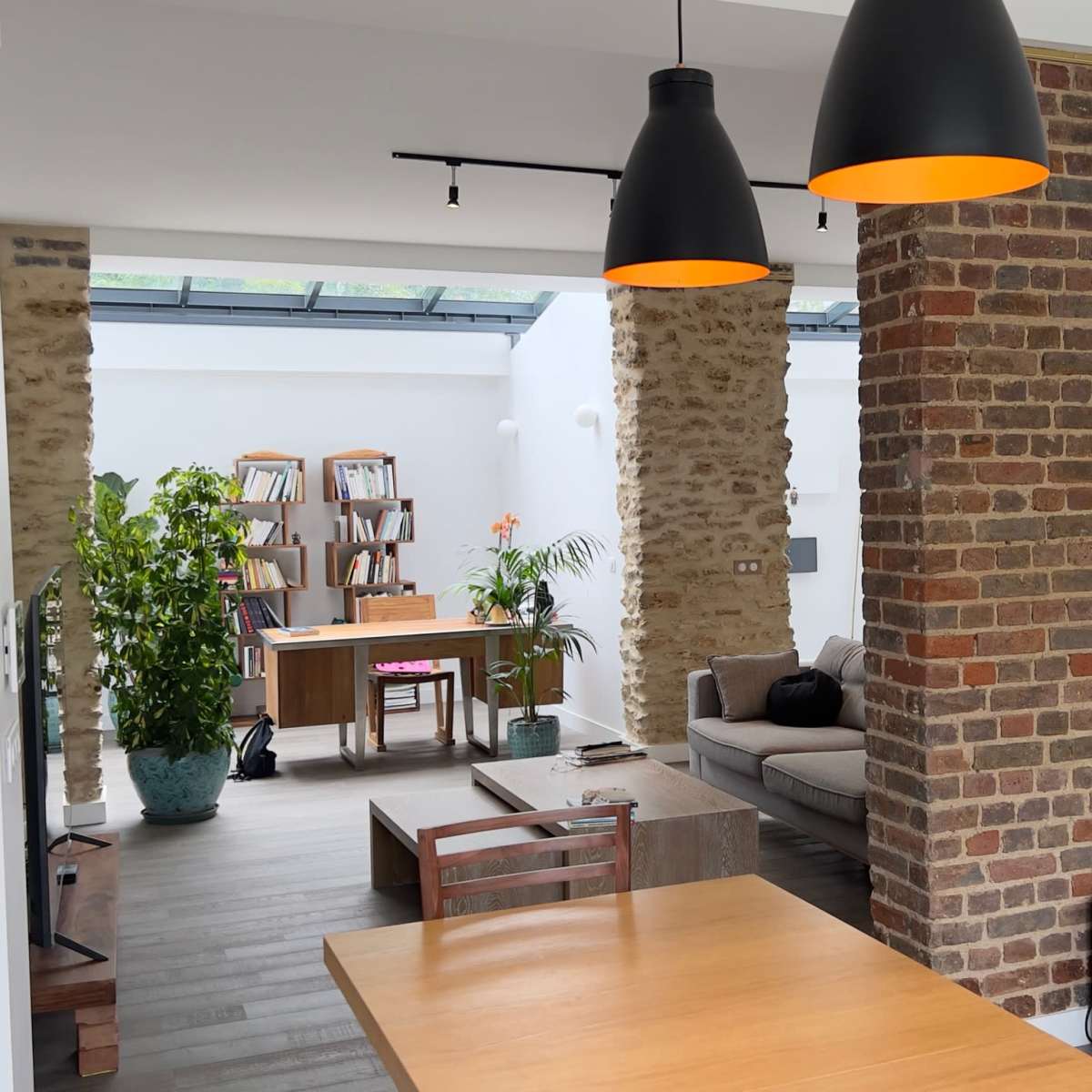 A modern living space featuring a combination of brick and neutral wall designs, with a sitting area, a staircase, and bookshelves visible in the background.