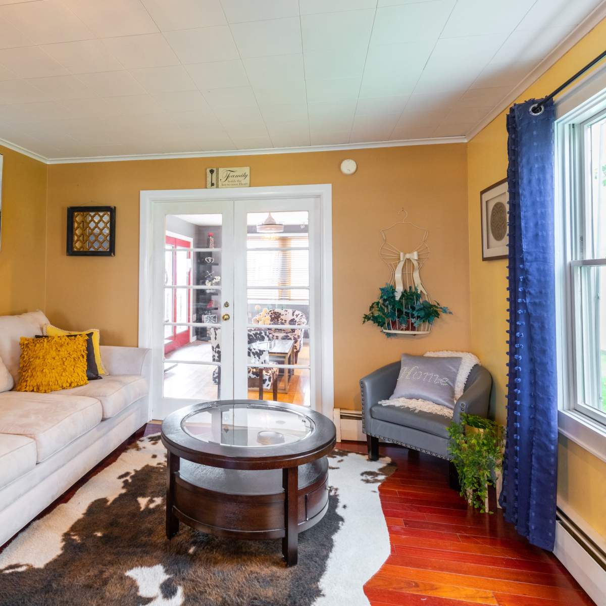 A cozy living room with a beige sofa, a round coffee table, and a large window letting in natural light.