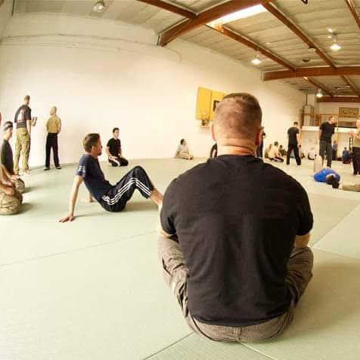 A group of people practices martial arts on mats in a spacious training facility.