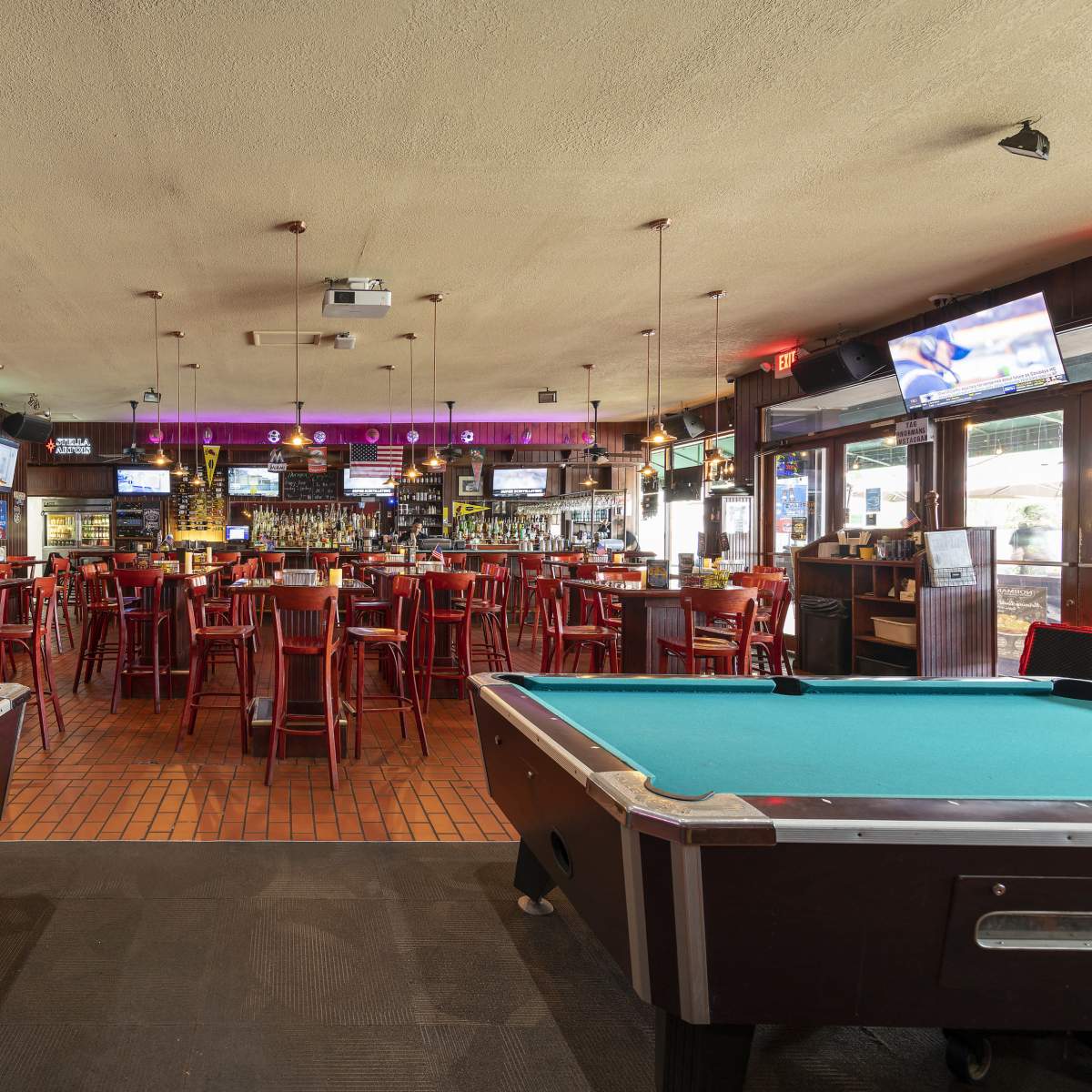A spacious bar and pool hall with two pool tables in the foreground and a seating area filled with tables and chairs in the background.