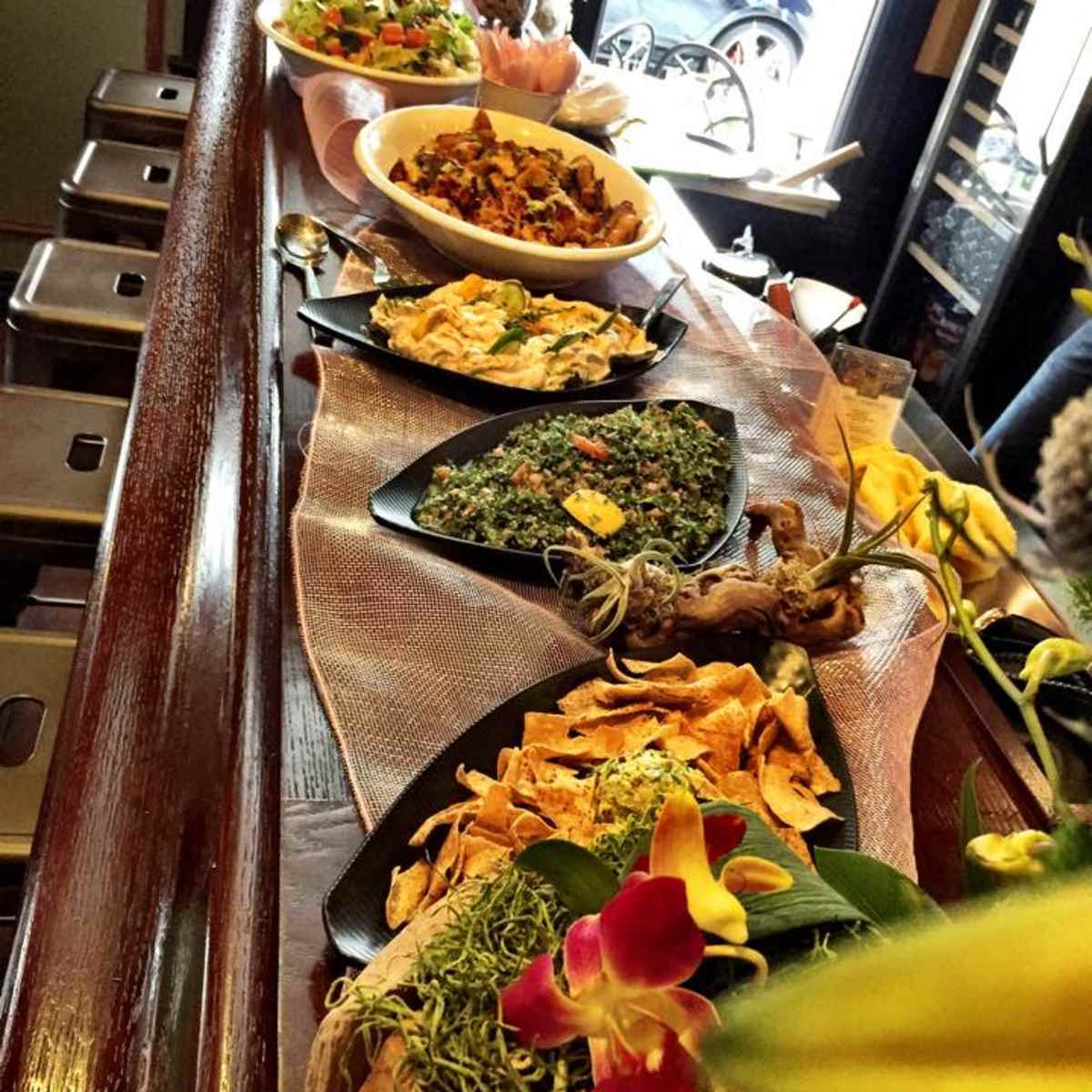 A variety of dishes, including salads and appetizers, are displayed on a wooden bar counter adorned with decorative elements.
