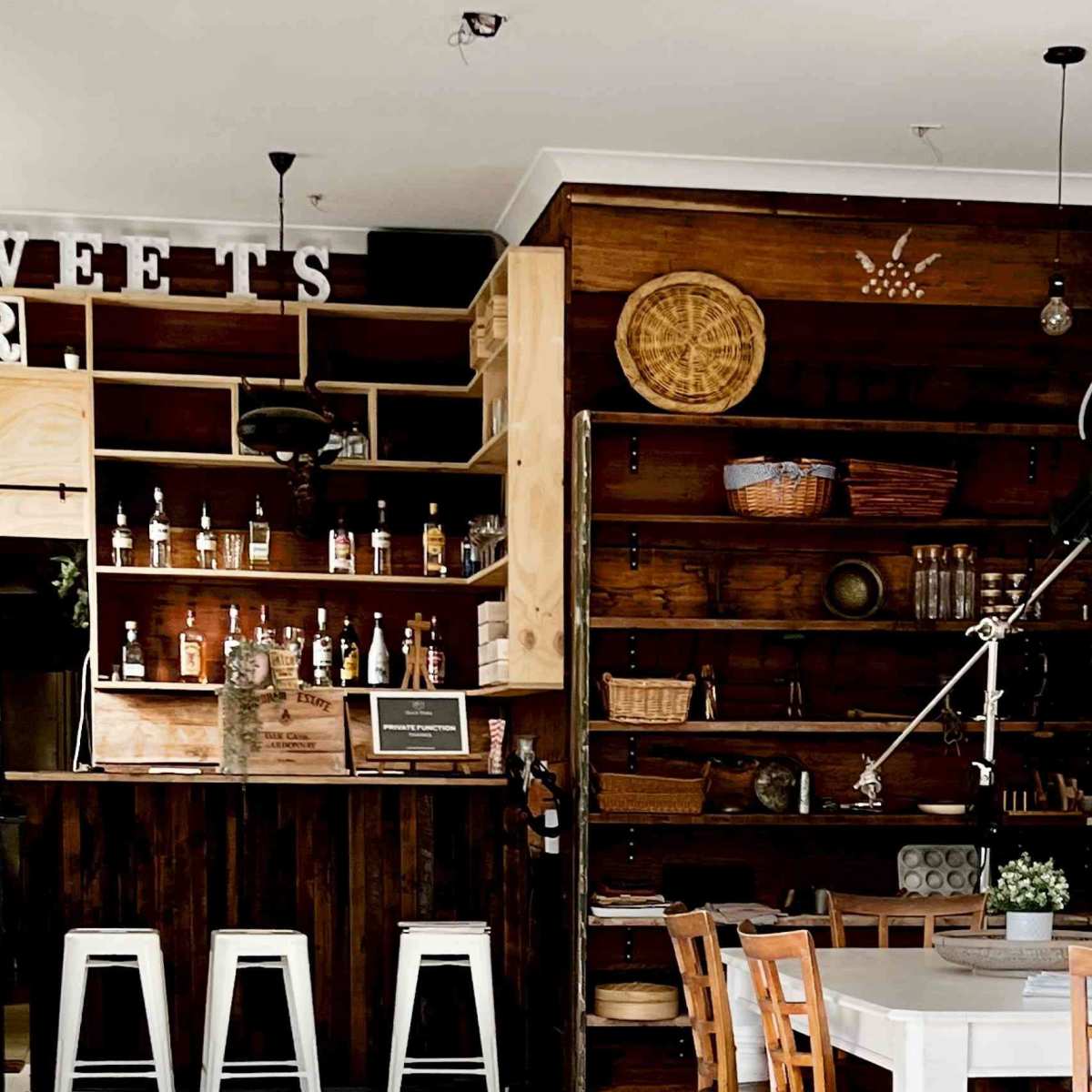 A rustic bar area with wooden shelves displaying bottles and decorative items, accompanied by a white dining table and chairs.