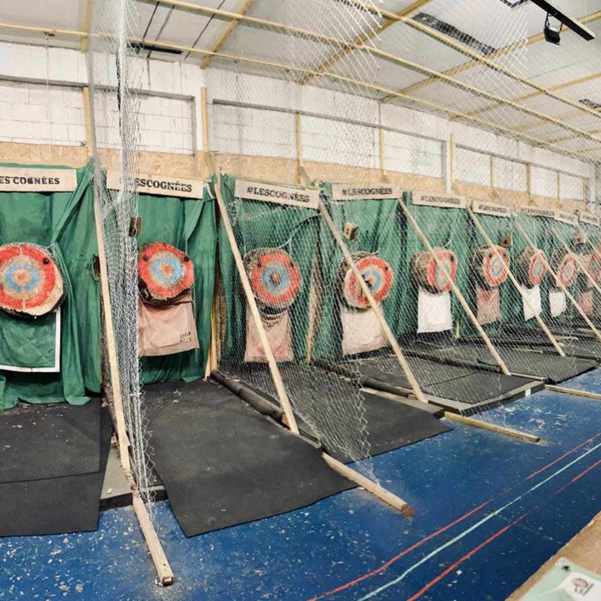 A series of target lanes for axe throwing, each with a segmented target mounted on a structure, all enclosed by nets.